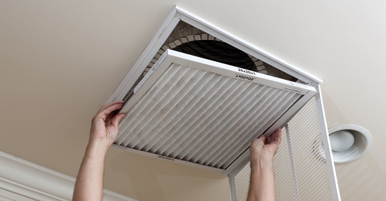 person replacing HVAC air filter in ceiling